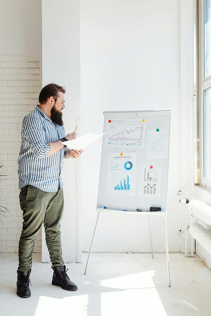 pexels-photo-7876386-7876386 Bearded man reviewing financial charts in sunlit office space.